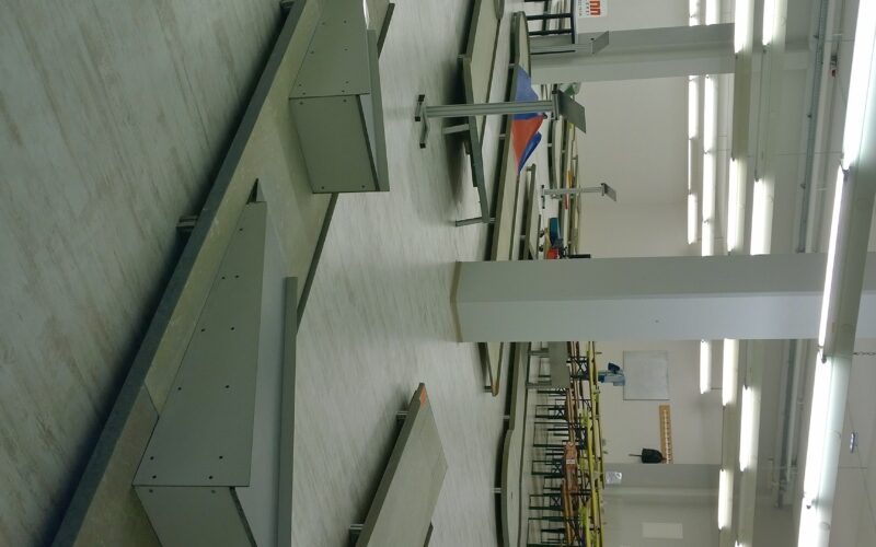 Eine Indoor-Minigolfanlage mit mehreren Bahnen, Hindernissen und Tischen in einem hell erleuchteten Raum mit weißen Wänden und Deckenleuchten.