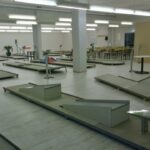Eine Indoor-Minigolfanlage mit mehreren Bahnen und Hindernissen, angrenzend an einen Sitzbereich mit Tischen und Stühlen unter heller Deckenbeleuchtung.