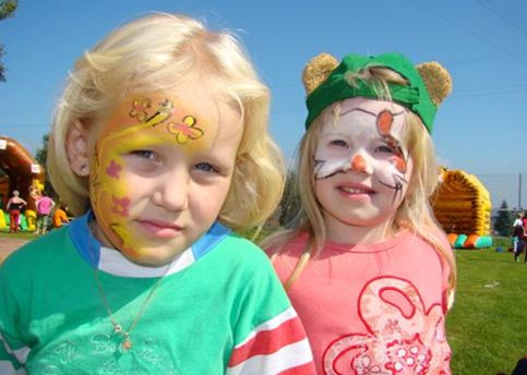 Zwei kleine Kinder mit Gesichtsbemalung stehen an einem sonnigen Tag im Freien, eines mit einem Schmetterlingsmotiv, das andere mit einem Katzengesicht und Bärenohren.