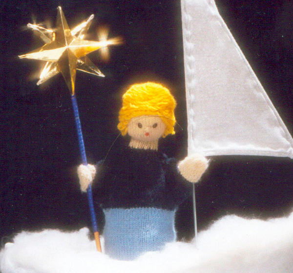 Eine handgefertigte Puppe mit gelbem Haar steht auf einer weißen, flauschigen Oberfläche und hält einen Sternenstab und eine weiße Fahne vor einem dunklen Hintergrund.