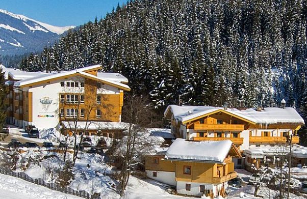 Schneebedeckte Holzhütten am Rande eines dichten Kiefernwaldes in einer bergigen Gegend, mit blauem Himmel über dem Kopf.