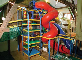 Indoor-Spielplatz mit einer großen roten Spiralrutsche, Klettergerüsten, Sicherheitsnetzen und verschiedenen Spielgeräten in einem hellen Raum.