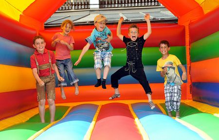 Fünf Kinder springen und spielen in einer bunten, aufblasbaren Hüpfburg.