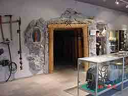 Eine Museumsausstellung mit einem rekonstruierten Mineneingang, Vitrinen mit Artefakten und an der Wand montierten Bergbauwerkzeugen.