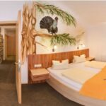 Ein Hotelzimmer mit einem Doppelbett, orangefarbenem Bettzeug, einem roten Sofa und einem Wandbild mit einem Vogel auf einem Ast über dem Bett.