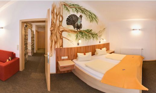 Ein Hotelzimmer mit einem Doppelbett, orangefarbenem Bettzeug, einem roten Sofa und einem Wandbild mit einem Vogel auf einem Ast über dem Bett.