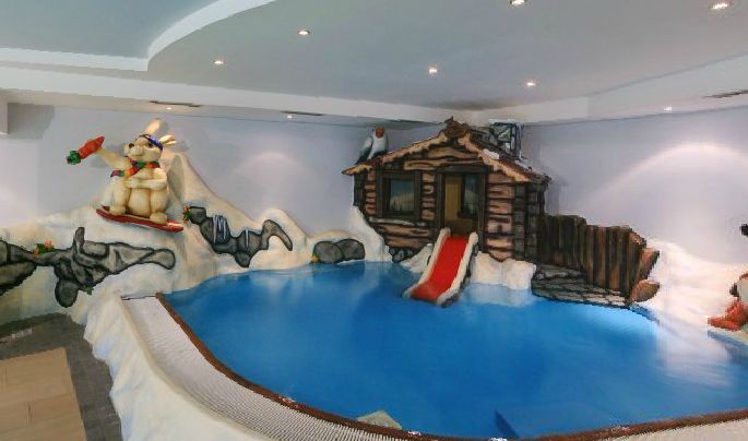 Kinderhallenbad mit einem verschneiten Bergthema, mit einem Bären auf Skiern, einer Holzhütte, einer roten Rutsche und dekorativem Schnee und Tieren.