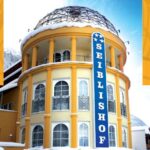 Ein rundes, gelbes Gebäude mit gewölbten Fenstern, einem Kuppeldach und einem vertikalen blauen Schild mit der Aufschrift "Seiblishof", mit Schnee auf dem Dach.