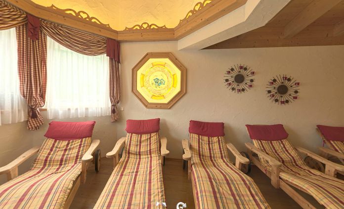 Eine Reihe von hölzernen Lounge-Sesseln mit karierten Kissen und roten Kopfstützen steht in einem gemütlichen Raum mit dekorativer Wandkunst, Vorhängen und einem Buntglasfenster.