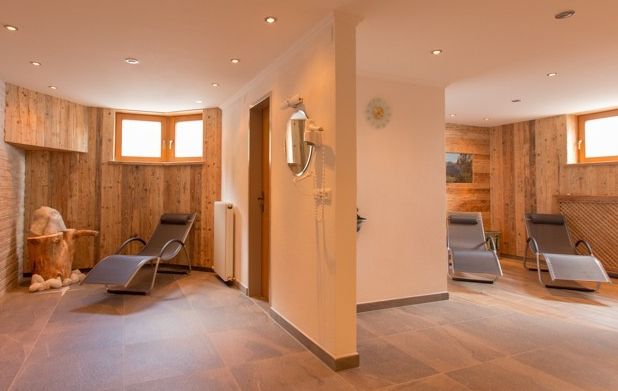 Ein Spa-Ruheraum mit Holzwänden, Liegestühlen, einem kleinen Holztisch und sanfter Beleuchtung schafft eine ruhige Atmosphäre.