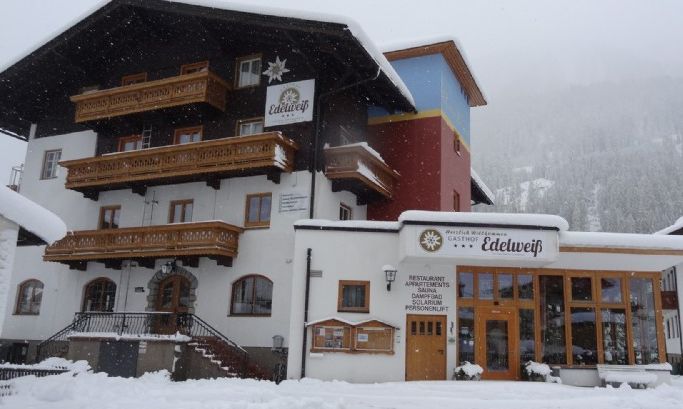 Ein verschneites, mehrstöckiges Alpenhotel mit Holzbalkonen und einem Schild mit der Aufschrift "Edelweiss" an der Fassade.