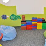 Ein Kinderspielzimmer mit bunten Schaumstoffblöcken, Sitzsäcken, an der Wand befestigtem Spielzeug und verspielten Wanddekorationen in Form von Fischen.
