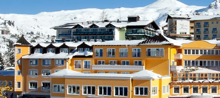 Eine Gruppe farbenfroher Gebäude mit schneebedeckten Dächern steht vor der Kulisse verschneiter Berge unter einem klaren Himmel.