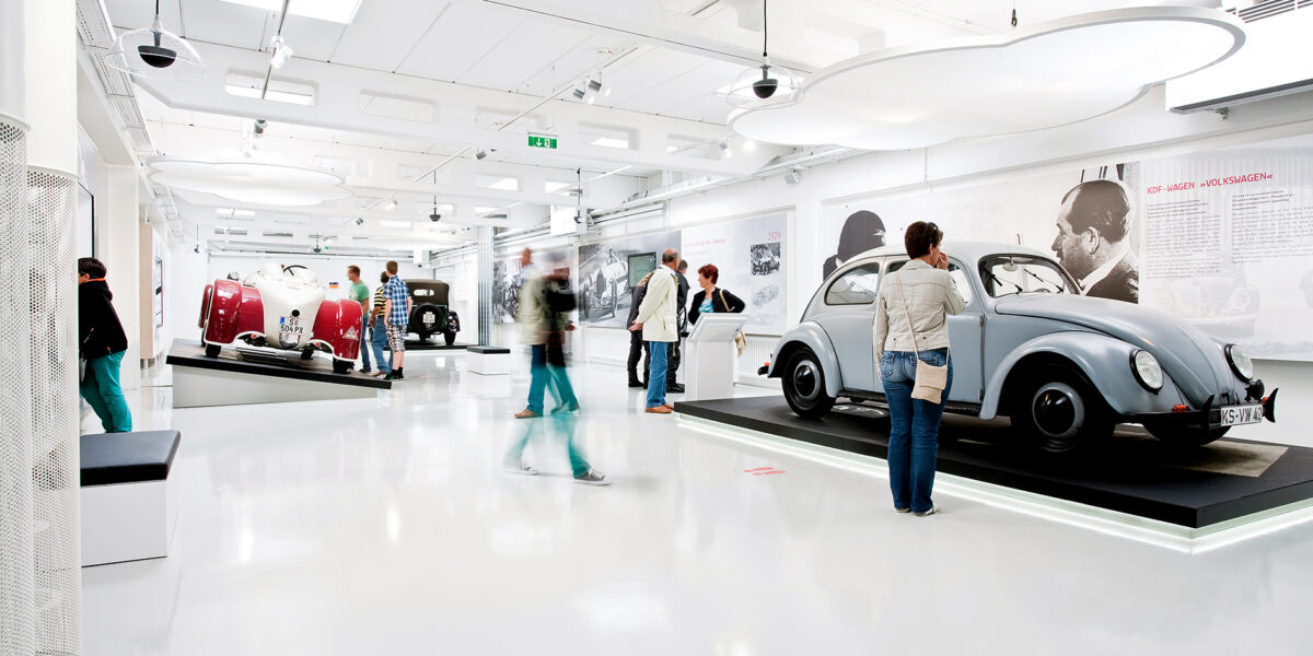 Menschen betrachten Oldtimer in einer hellen, modernen Ausstellung im Automobilmuseum mit weißen Böden und Wänden.