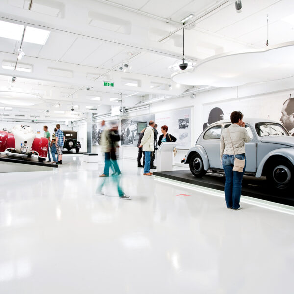 Menschen betrachten Oldtimer in einer hellen, modernen Ausstellung im Automobilmuseum mit weißen Böden und Wänden.