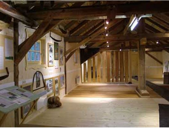 Ausstellungsraum mit Holzböden und -balken, Informationstafeln an den Wänden, Vitrinen und warmer Beleuchtung.