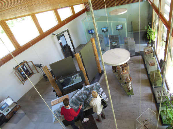 Zwei Personen betrachten ein großes topografisches Modell in einer modernen, gut beleuchteten Museumsausstellung mit Glasvitrinen, Karten und Informationstafeln.