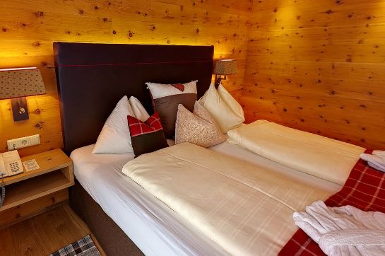 Ein ordentlich gemachtes Doppelbett mit mehreren Kissen und einer rot karierten Decke in einem holzgetäfelten Raum mit Wandlampen und einem Nachttisch.