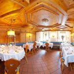 Ein warm beleuchtetes Restaurant mit holzgetäfelten Wänden und Decken, gefliestem Boden, blauen gepolsterten Bänken und Tischen mit weißen Tischdecken und Servietten.