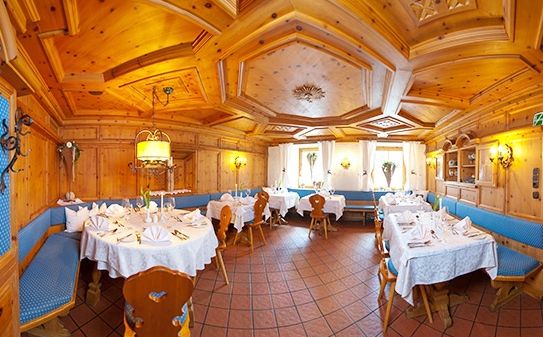 Ein warm beleuchtetes Restaurant mit holzgetäfelten Wänden und Decken, gefliestem Boden, blauen gepolsterten Bänken und Tischen mit weißen Tischdecken und Servietten.