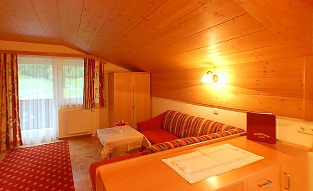 Gemütliches Zimmer mit holzgetäfelter Decke, rot gestreiftem Sofa, kleinem Tisch, Kleiderschrank und großem Fenster mit Vorhängen, die Tageslicht hereinlassen.