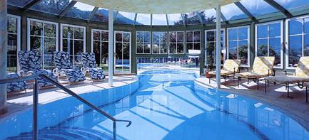 Hallenbadbereich mit Liegestühlen, großen Fenstern und einer Glasdecke, die den Raum mit natürlichem Licht erfüllt.