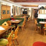 Ein gemütliches Restaurant mit Holzmöbeln, grün gepolsterten Sitzgelegenheiten, dekorierten Tischen und traditioneller alpiner Einrichtung.