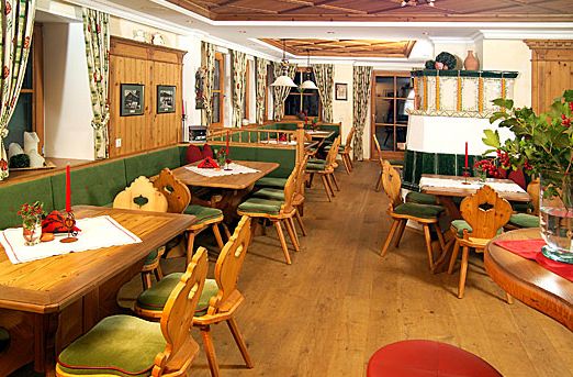 Ein gemütliches Restaurant mit Holzmöbeln, grün gepolsterten Sitzgelegenheiten, dekorierten Tischen und traditioneller alpiner Einrichtung.
