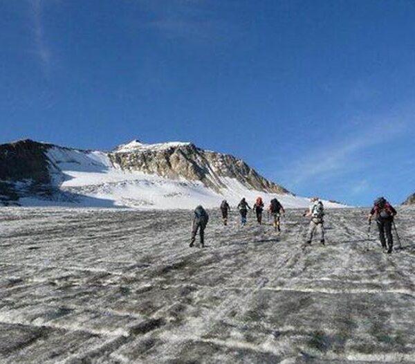 Eine Gruppe von Bergsteigern wandert über einen Gletscher zu einem schneebedeckten Berg unter einem strahlend blauen Himmel.