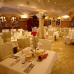 Eleganter Speisesaal eines Restaurants mit ordentlich gedeckten Tischen, weißen Tischdecken und dekorativen Elementen an Wänden und Tischen, bereit für Gäste.