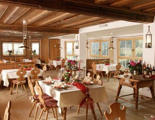 Ein gemütlicher Speisesaal mit Holzböden und -decken, gedeckten Tischen mit Blumen und großen Fenstern, die viel Tageslicht hereinlassen.