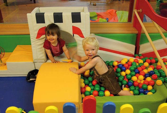 Zwei kleine Kinder spielen in einer mit bunten Plastikbällen gefüllten Ballgrube, umgeben von weichen Spielgeräten.