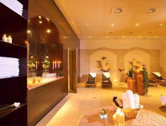 Eine Spa-Lounge mit Liegestühlen, gerollten Handtüchern, brennenden Kerzen, Wandkunst und gedämpfter Beleuchtung, die eine entspannende und einladende Atmosphäre schafft.
