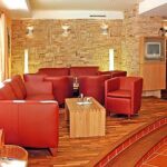 Ein modernes Wohnzimmer mit roten Ledersofas und -sesseln, einem hölzernen Couchtisch, Holzfußboden, einer Akzentwand aus Stein und einem kleinen Fernseher in der Ecke.