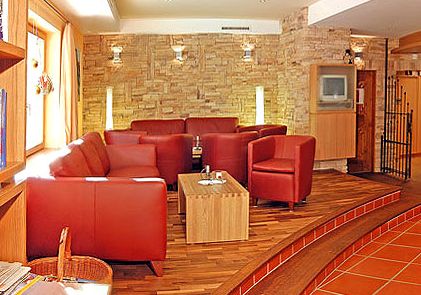 Ein modernes Wohnzimmer mit roten Ledersofas und -sesseln, einem hölzernen Couchtisch, Holzfußboden, einer Akzentwand aus Stein und einem kleinen Fernseher in der Ecke.