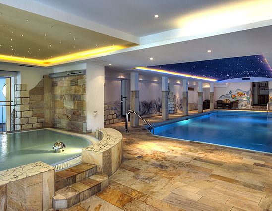 Wellnessbereich im Innenbereich mit einem runden Whirlpool und einem rechteckigen Schwimmbecken, mit Steinfliesenboden und einer Decke mit eingebauter Beleuchtung.