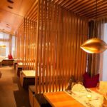 Modernes Restaurantinterieur mit Holztrennwänden, warmer Raumbeleuchtung und ordentlich gedeckten Tischen mit gefalteten Servietten und Speisekarten.