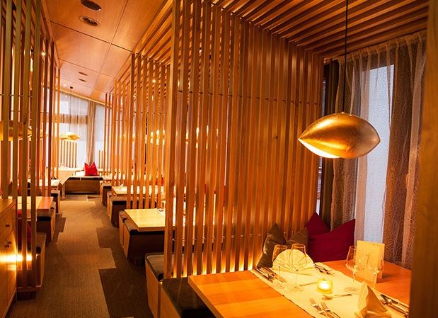 Modernes Restaurantinterieur mit Holztrennwänden, warmer Raumbeleuchtung und ordentlich gedeckten Tischen mit gefalteten Servietten und Speisekarten.