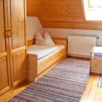 Holzgetäfeltes Schlafzimmer im Dachgeschoss mit zwei Einzelbetten, einem Holzschrank, gestreiften Teppichen, einem Heizkörper und einem Oberlichtfenster.