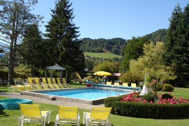 Swimmingpool im Freien mit gelben Liegestühlen, grünem Rasen, Bäumen und Hügeln im Hintergrund unter einem klaren blauen Himmel.