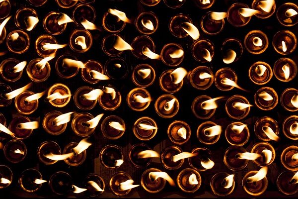Reihen kleiner Kerzen, die mit sichtbaren Flammen brennen, von oben in einer schwach beleuchteten Umgebung betrachtet.