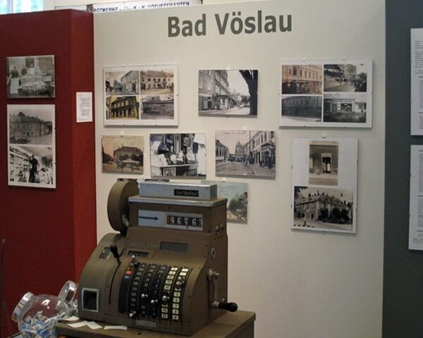 Ausstellungsdisplay für Bad Vöslau mit Vintage-Fotografien an der Wand und einer antiken Registrierkasse im Vordergrund.