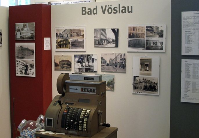 Ausstellungsdisplay für Bad Vöslau mit Vintage-Fotografien an der Wand und einer antiken Registrierkasse im Vordergrund.
