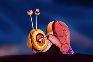 Eine Schneckenskulptur aus bemaltem Brot und Stöcken als Fühler, vor blauem Hintergrund.