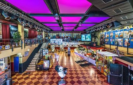 Farbenfrohes Interieur einer Kinolobby mit einem Kiosk, Filmplakaten an den Wänden und einer Treppe, die in eine obere Etage führt.