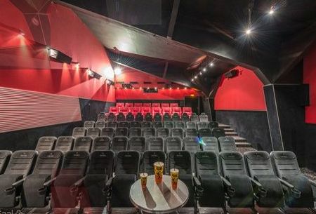 Ein kleines Kino mit Reihen schwarzer Sitze, roten und schwarzen Wänden und einem runden Tisch davor, auf dem vier Getränke stehen.