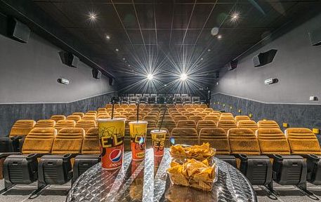 Weitwinkelansicht eines leeren Kinos mit gelben Sitzen, einem Tisch davor mit Getränken und Popcorn und hellen Lichtern, die den Raum erhellen.