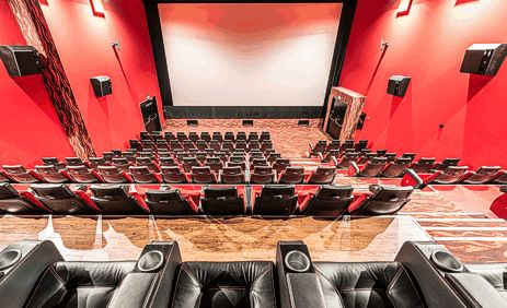 Leeres Kino mit roten Wänden, Reihen schwarzer Sitze, einer großen leeren Leinwand und Plüschsitzen im Vordergrund.