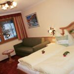 Ein gemütliches Hotelzimmer mit einem Doppelbett, einer grünen Couch, einem kleinen runden Tisch, einem Fenster mit Winterblick und zwei roten Rosen auf dem Bett.