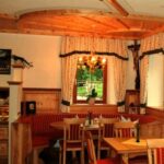 Ein gemütlicher Essbereich mit Holzmöbeln, roten gepolsterten Bänken, einem Fenster mit Vorhängen, einem Kronleuchter und einem Kruzifix an der Wand.